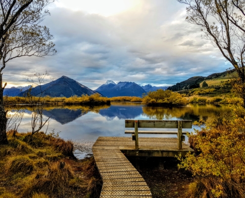 Bench facing lagoon with mountains reflected and trees all yellow in autumn
