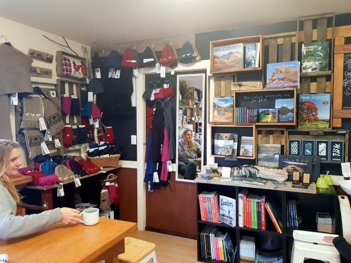 Lady sat at table with drink in shop with books and wool accessories displayed