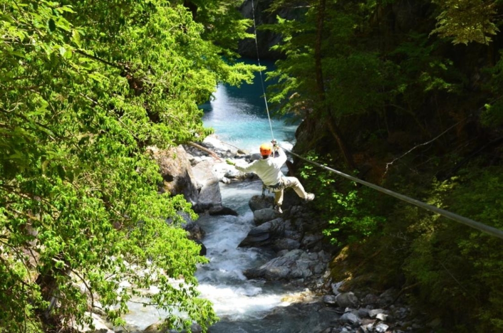 Back of person ziplining over river through forest