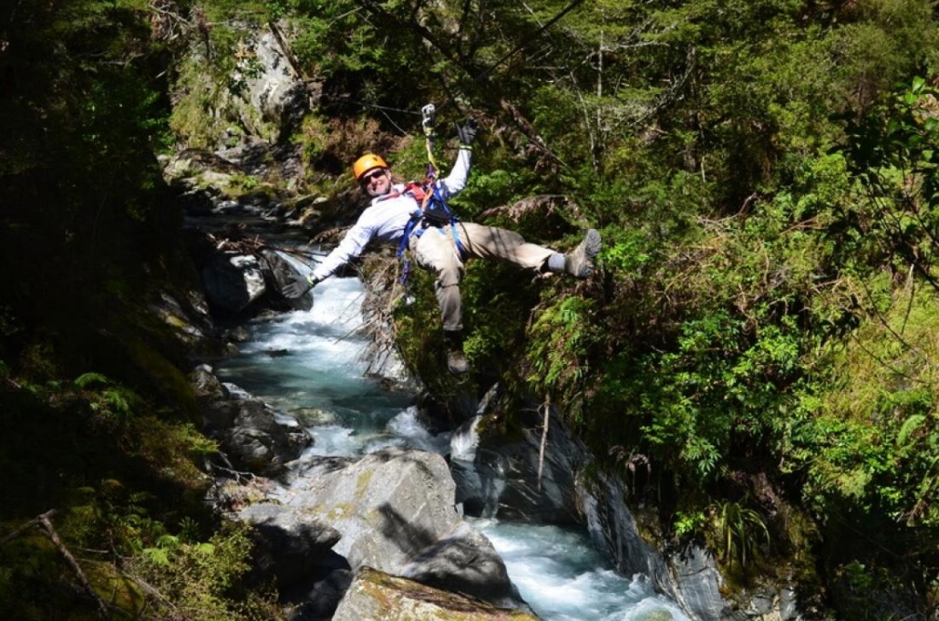 Man smiling while ziplining over river through forest