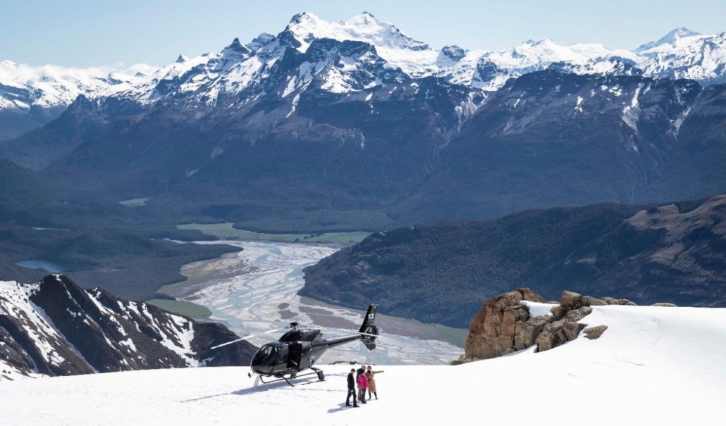Helicopter landed on snow topped mountain with people walking near it