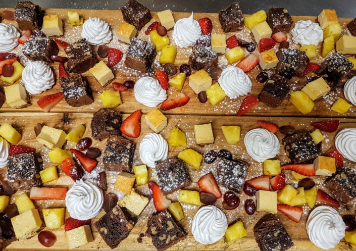 Bites of brownies, cheesecake, meringues and pineapple and strawberries on wooden platters