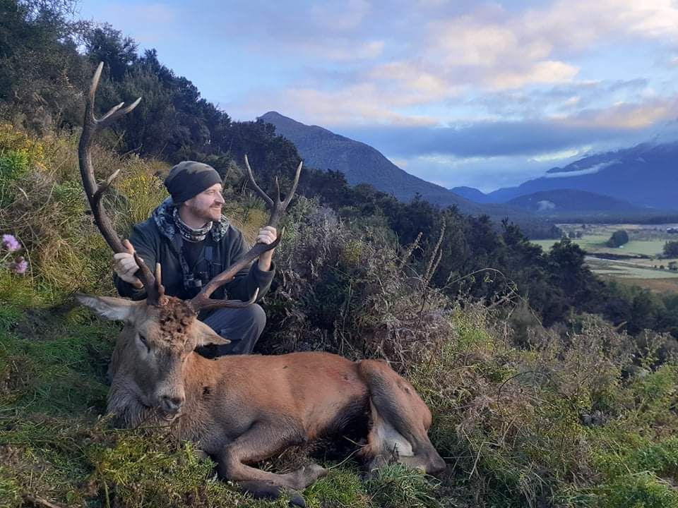 Man holding up antlers of dead deer on the side of a mountain