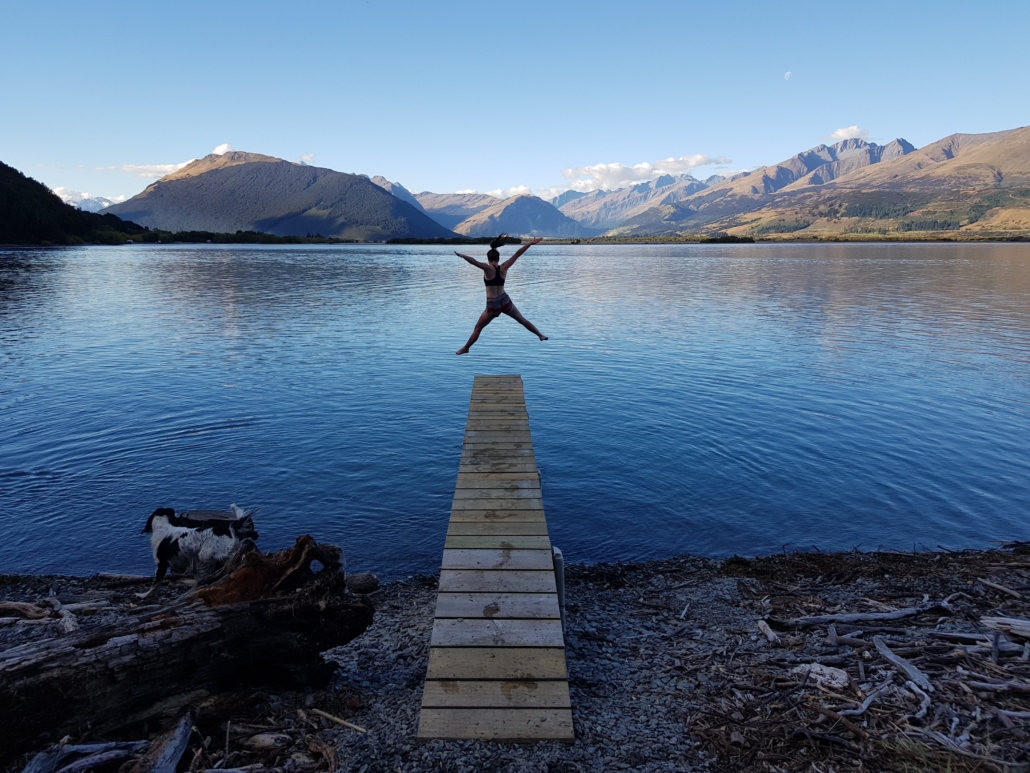 Woman jumping off wharf into lake surrounded by mountains