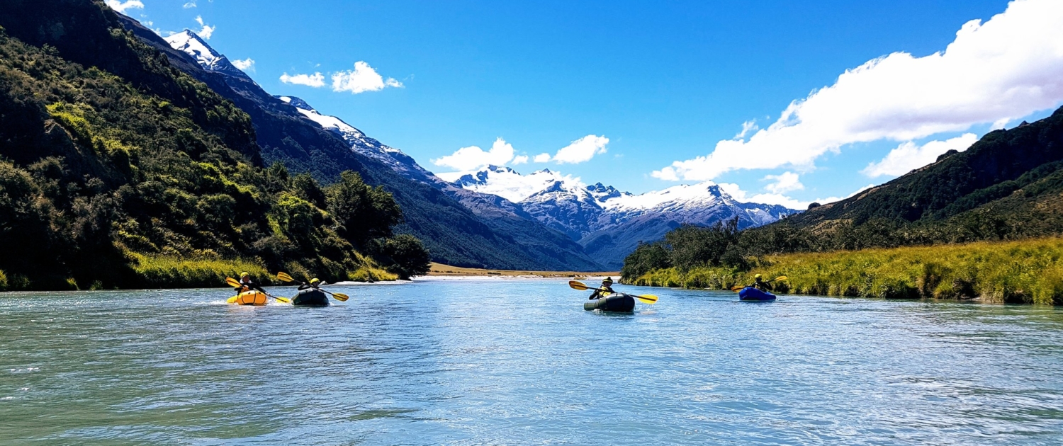 4 packrafts on the river in front of mountains and blue sky