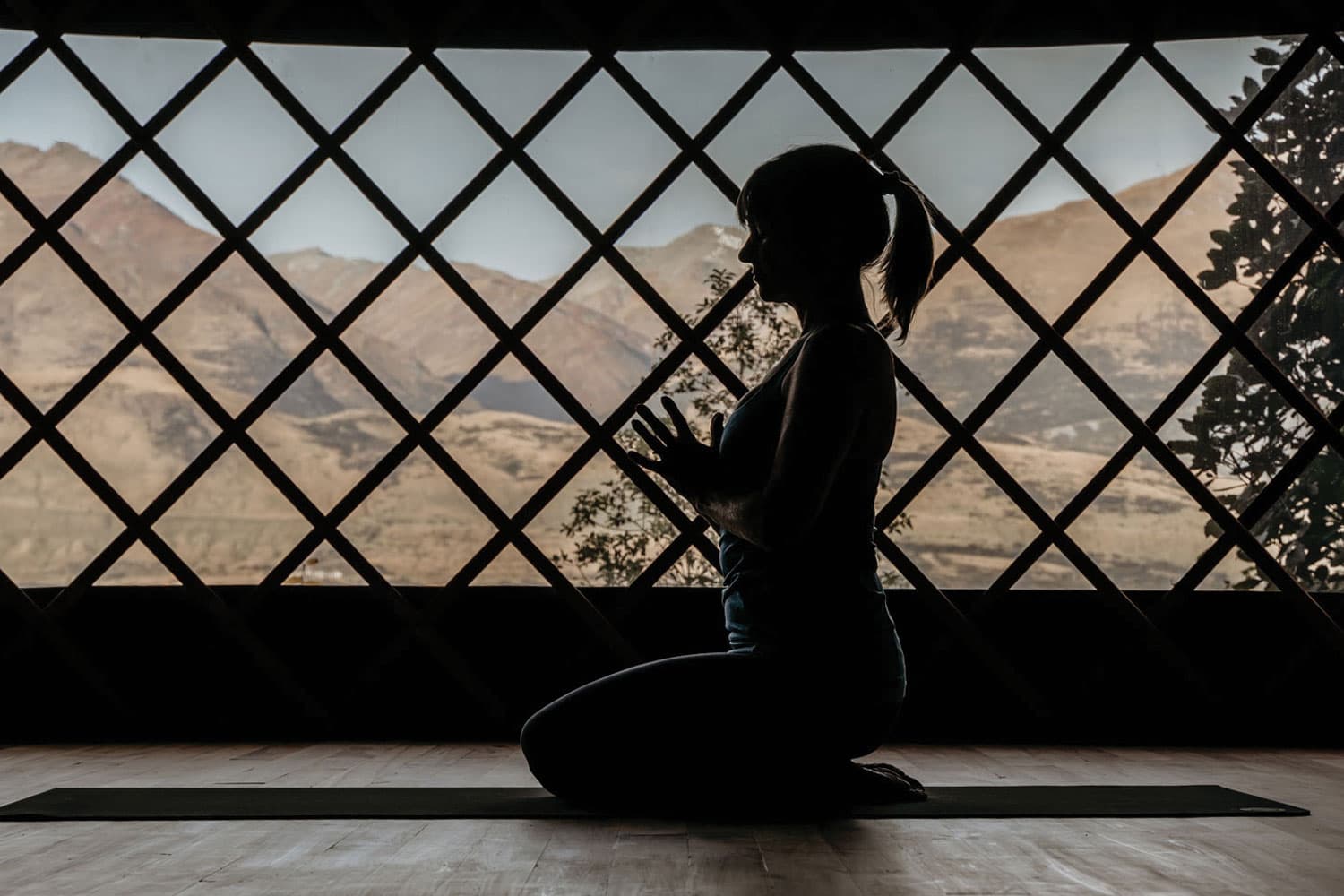Yoga student kneeling with hands together in yurt in front of mountain view