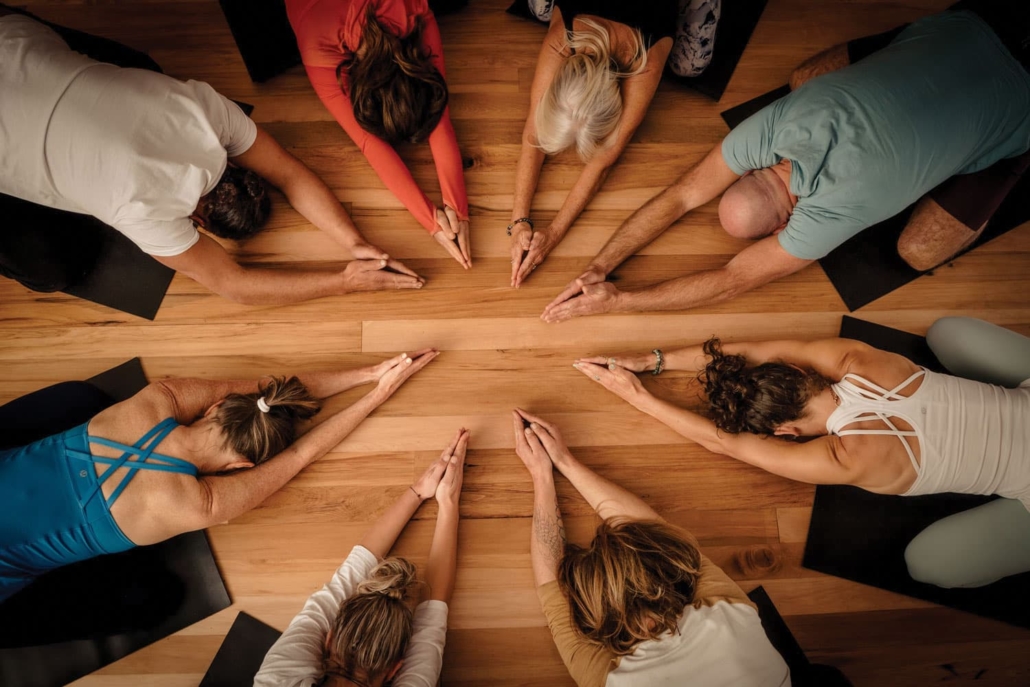 Yoga class with everyone lying on their fronts in a circle and hands together with arms stretched out